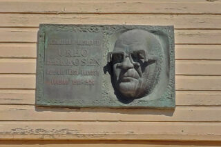 Talon ulkoseinässä oleva reliefi. Reliefissä on kuva Kekkosesta sekä teksti "Tasavallan Presidentti Urho Kekkosen koti oli tässä talossa vuosina 1911-1926"