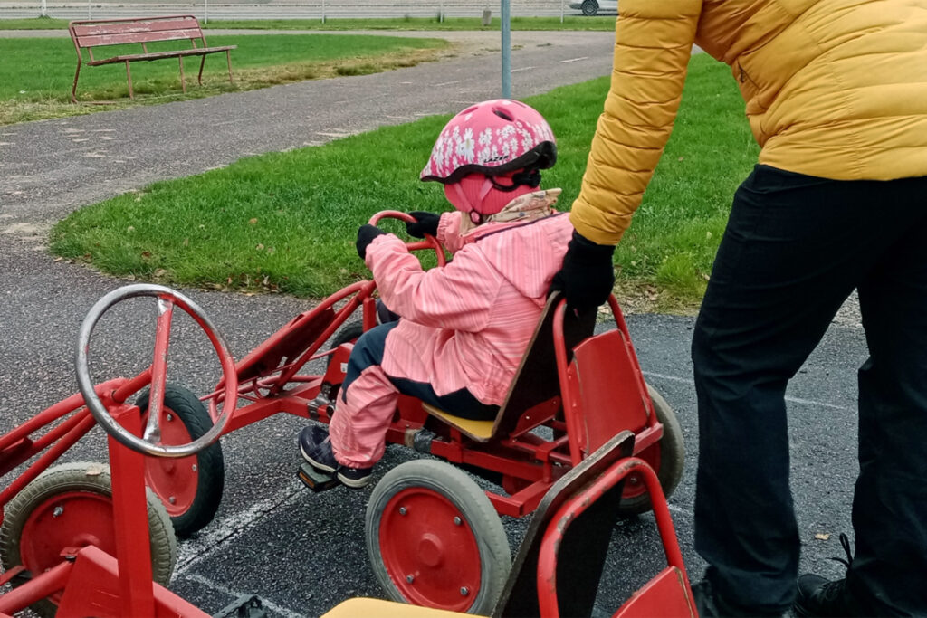 Tyttö lähdössä ajelulla polkuautolla aikuisen opastuksella