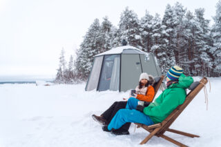 Lämpimät juomat iglun edustalla nauttien ja talvista Oulujärveä ihaillen