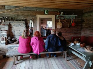 People sitting on a bench in Pihlajamäki House at Riihipiha Museum